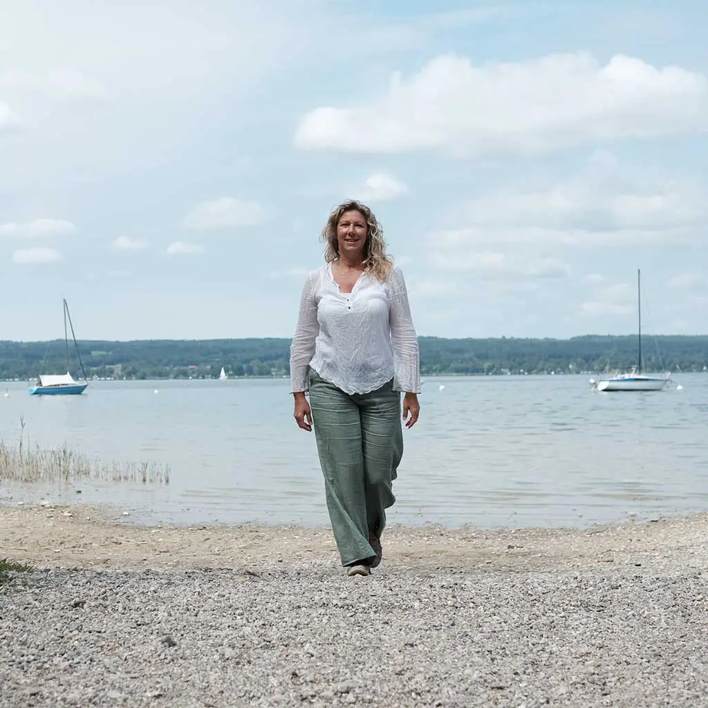 Frau läuft über Kiesstrand mit Meer im Hintergrund.