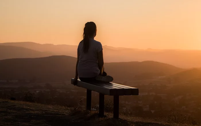 Frau sitzt auf einer Bank beim Sonnenuntergang.